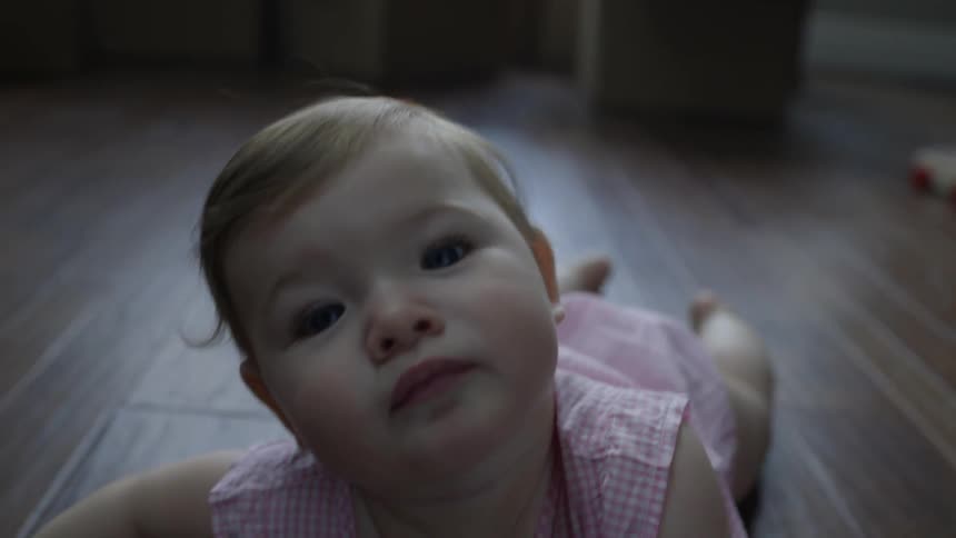 Baby girl resting on stomach on hardwood floor in home
