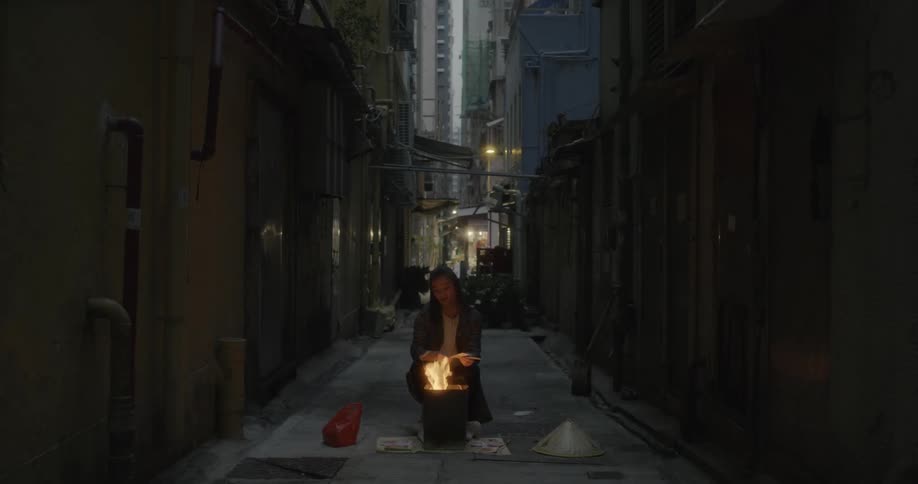 A woman lights a fire in a bucket in the alley