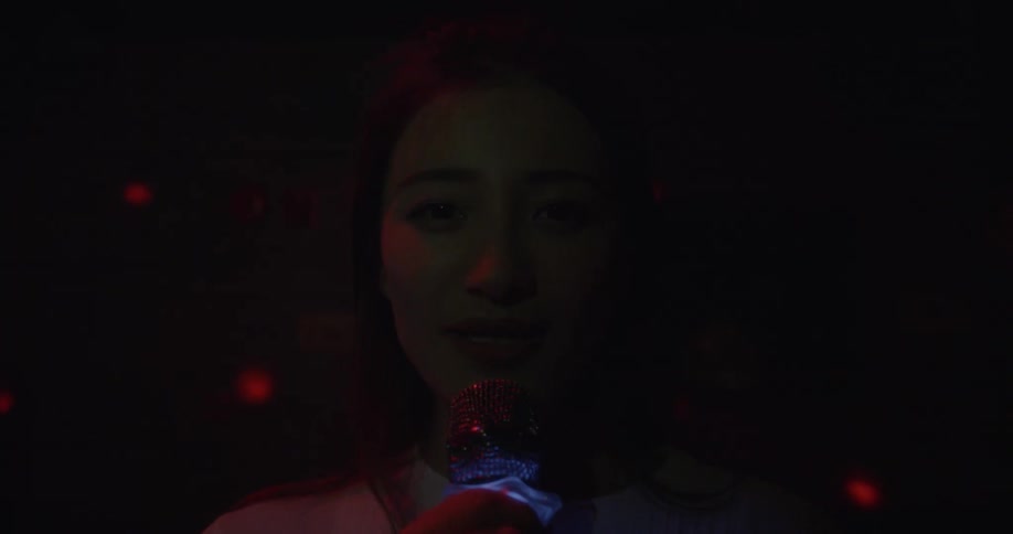 A woman smiles while singing karaoke in a dark room