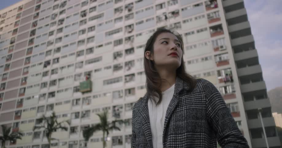 A woman is looking around in front of a building on a windy day
