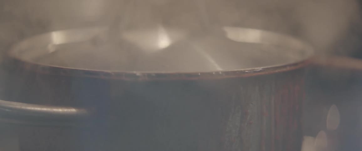 Steam and bubbles coming out from under lid on boiling pot