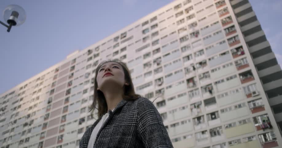 A woman is standing in front of a building on a sunny day looking around