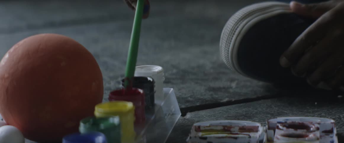Child dipping paint brush into container of red paint