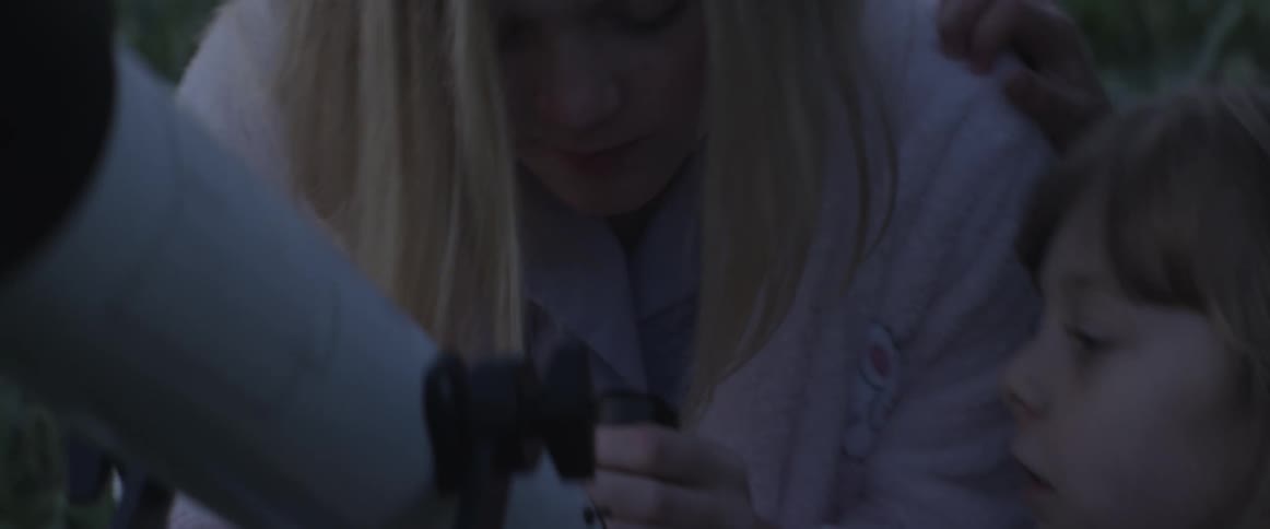 A woman looks through a telescope with a child
