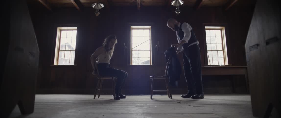 A man carries a chair over to a woman tied to a chair