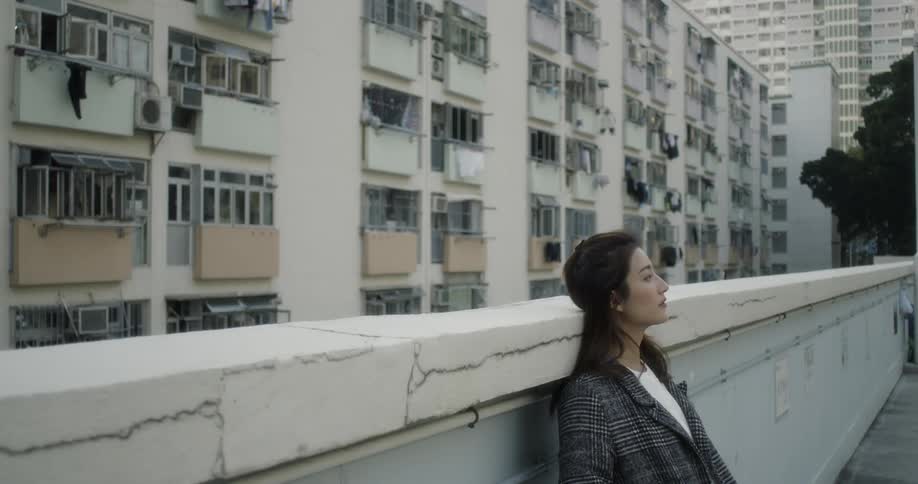 A woman leans against the wall looking up at the sky