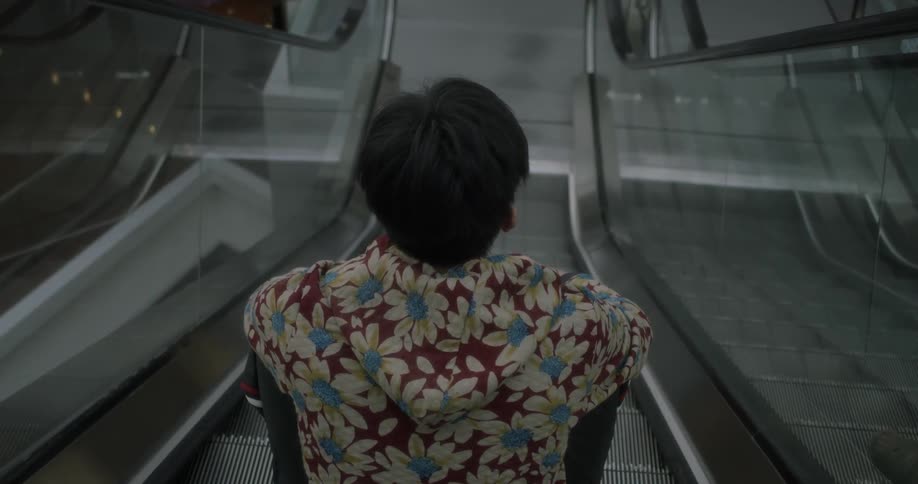 A man in a floral shirt sits on a moving escalator
