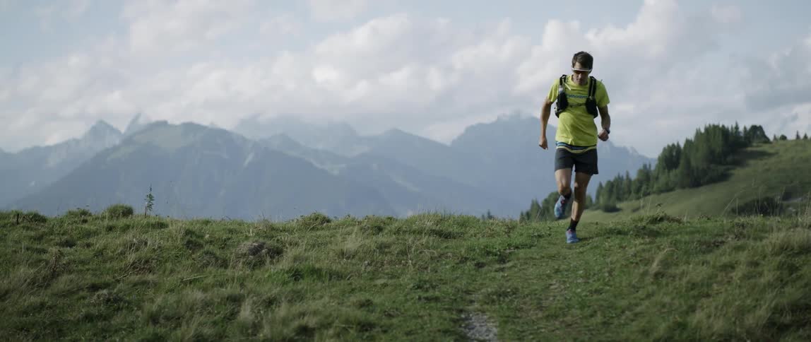 A man runs a hilly trail on a sunny day