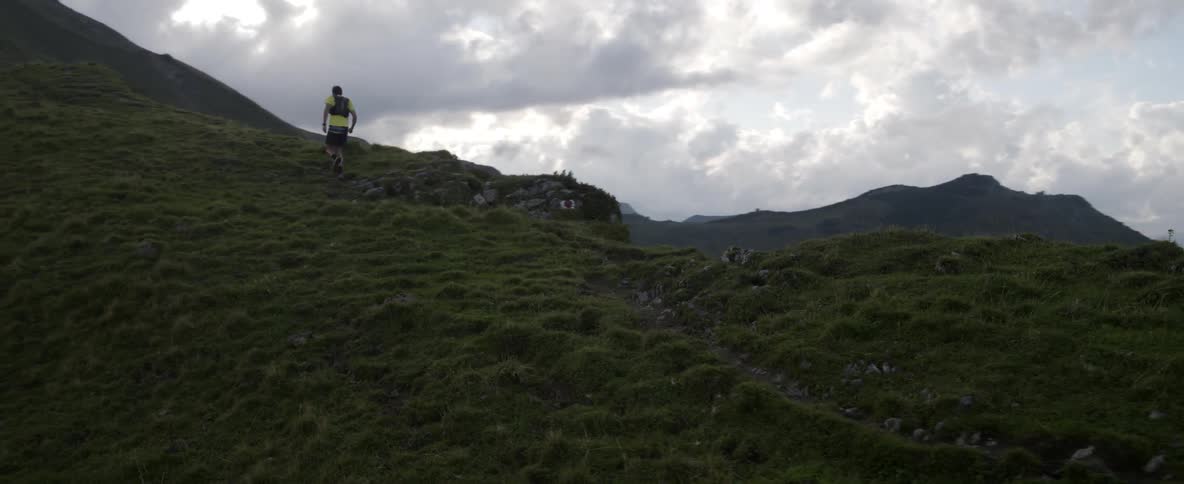 Man jogs up a grassy mountain on a cloudy day
