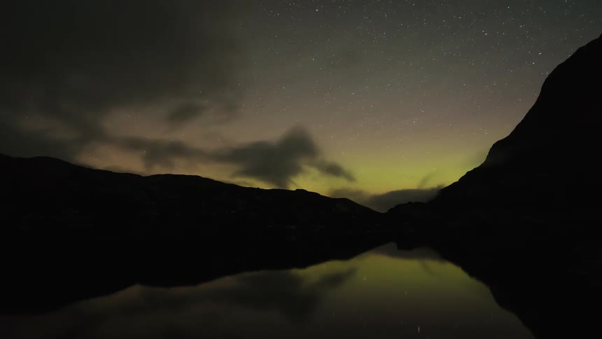 Clouds pass above a mountain lake at night