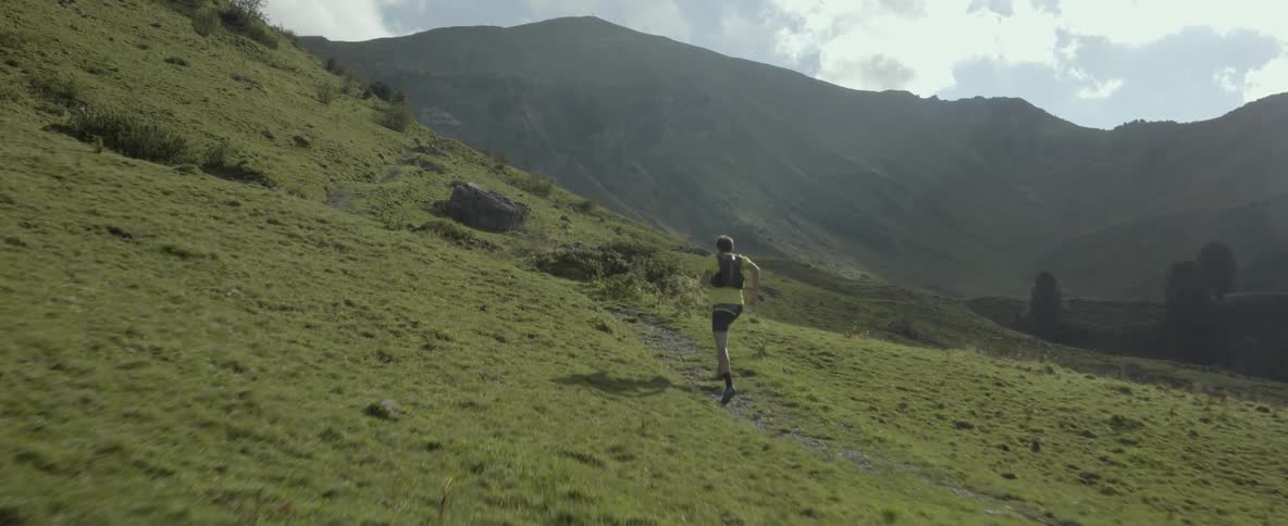 A man jogs up a grassy mountain trail