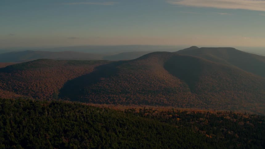 The long range of mountains are covered with trees at sunset