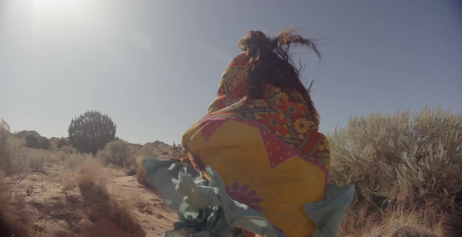 A woman wearing long robes walks in the desert