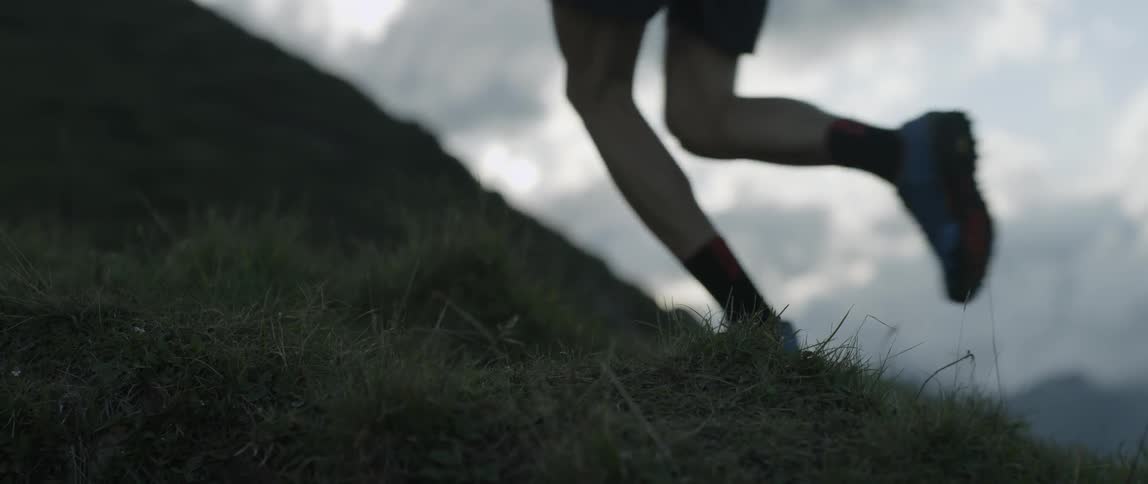 Man jogs up a grassy mountain on a cloudy day