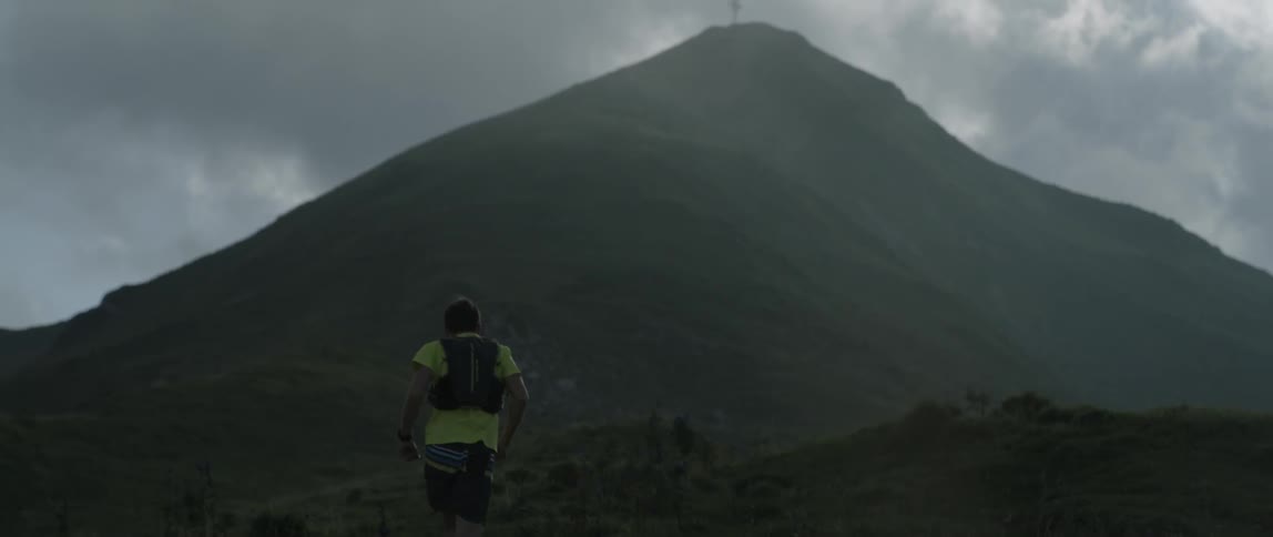 A man jogs up a mountainside towards a cross on the peak