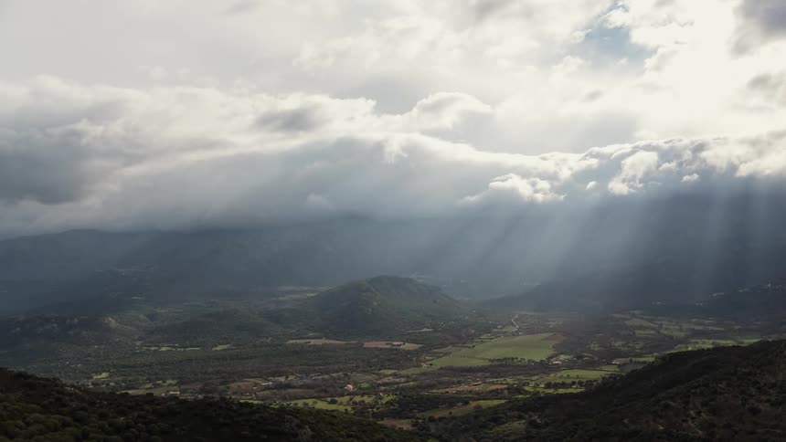 Clouds pass above a mountain and farms in a green valley