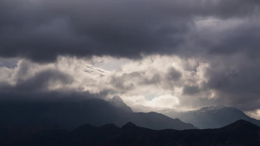 Dark broody clouds roll over a mountain range during the day