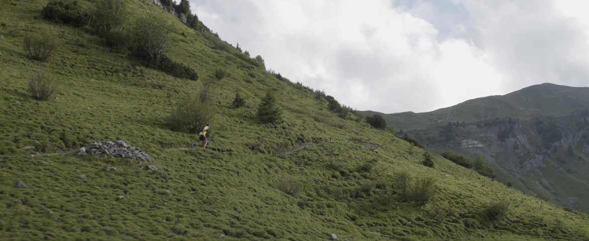 Man jogs up a grassy mountain on a cloudy day