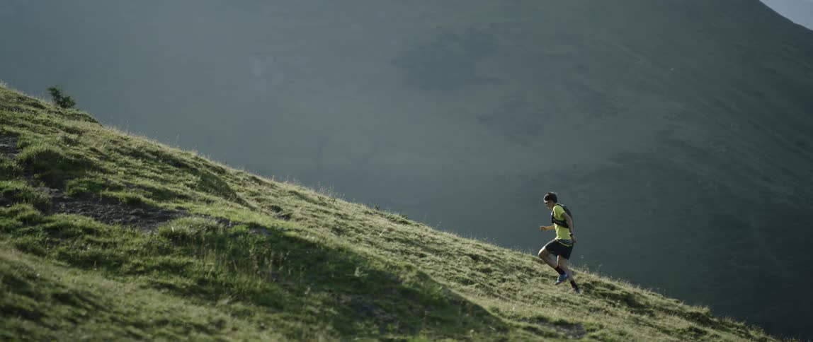 A man jogs up a grassy mountainside