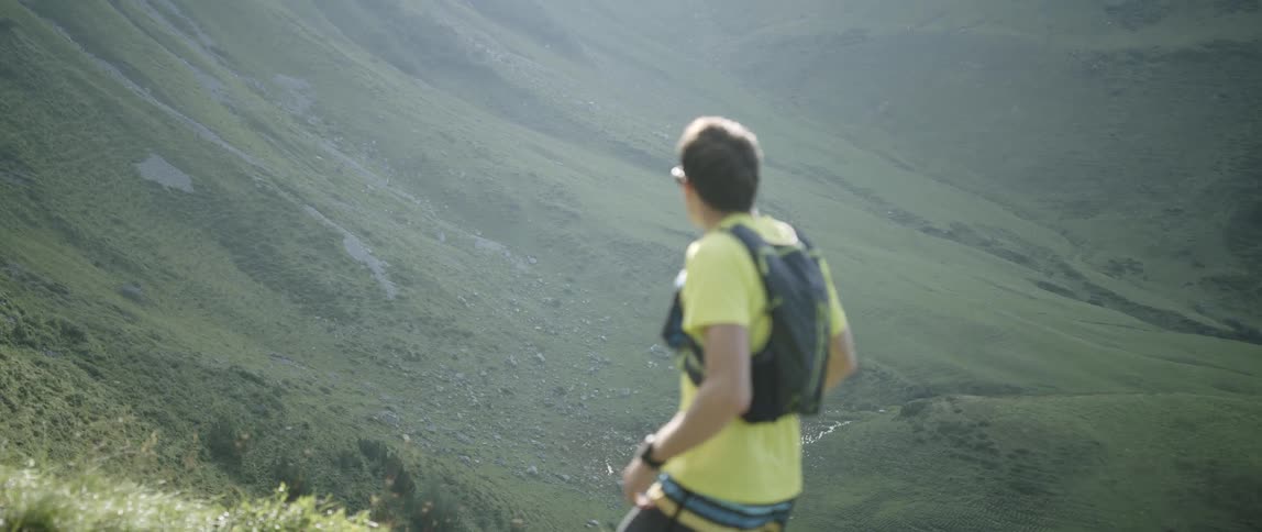 A man hiking up a mountain during the day stops to take in the view