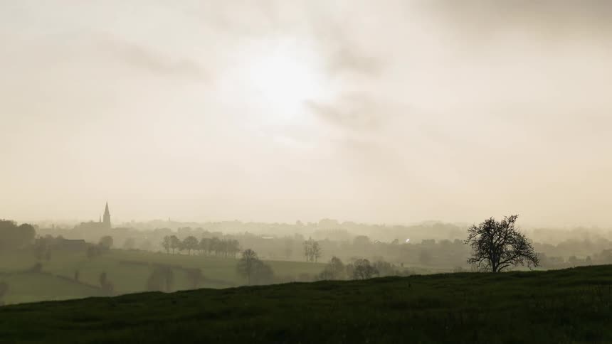 Clouds pass above a misty hilly landscape