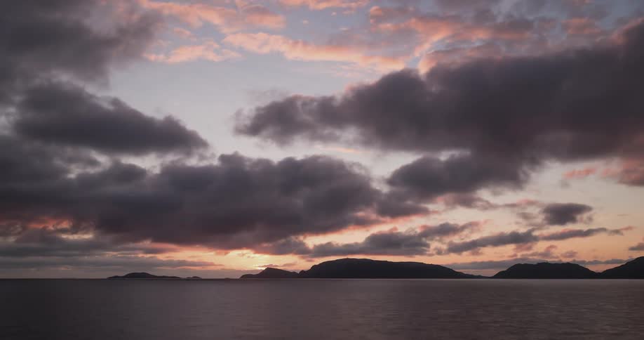 Clouds float over the sea and mountains at sunset