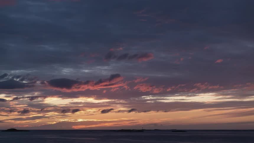 Clouds pass above flowing ocean water at sunset