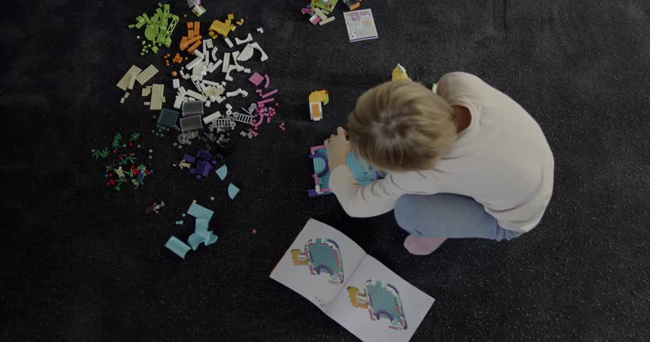A child is crouching on the carpet building legos