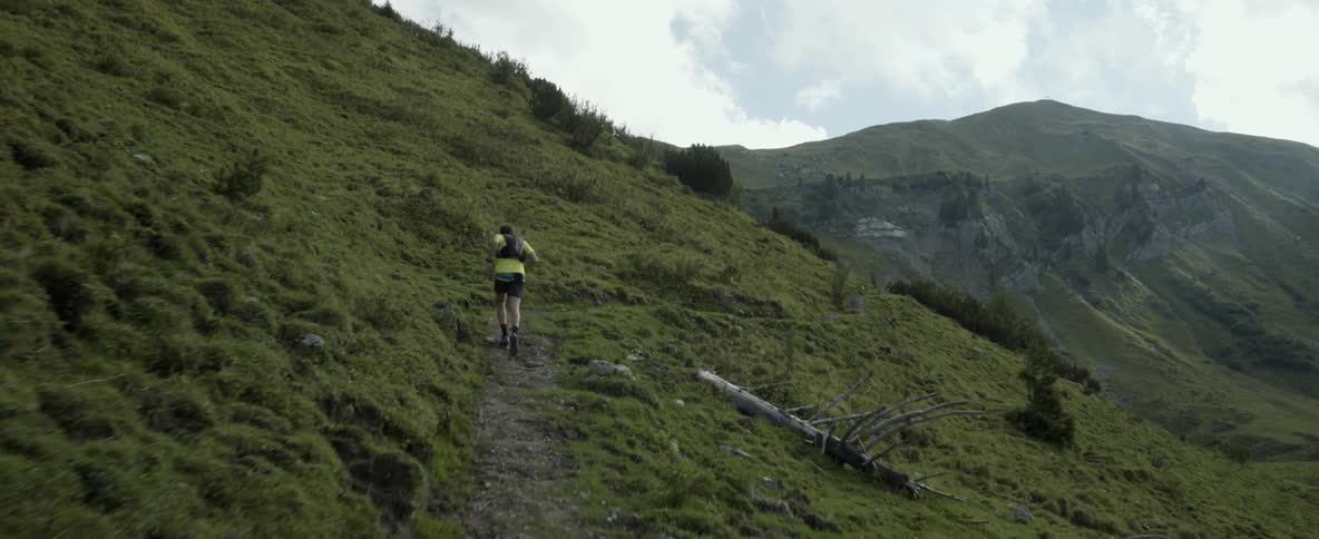 A man is jogging on a dirt path up a hill on a cloudy day
