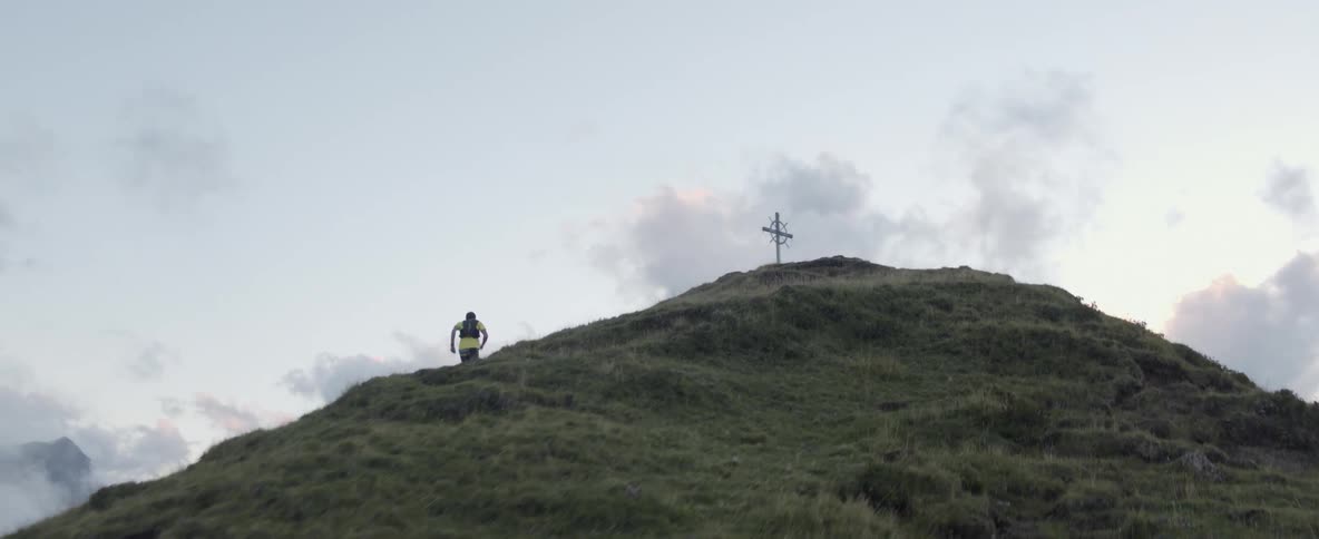 A man runs up a mountainside towards a cross