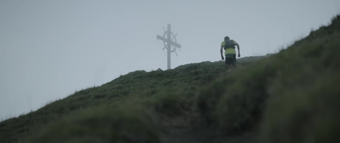 Man jogs up a grassy mountain on a cloudy day