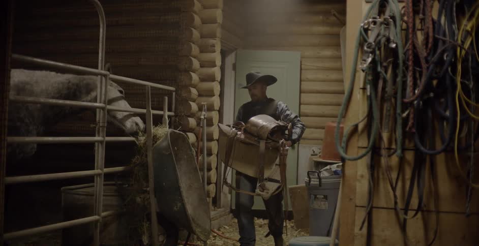 A man carries a saddle into a barn