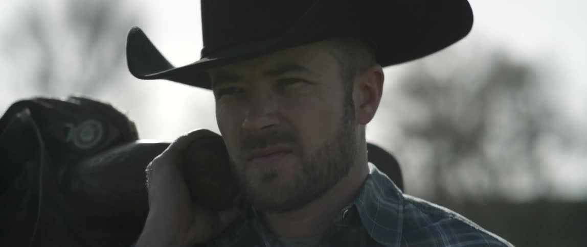 A cowboy carries a saddle outside on a sunny day