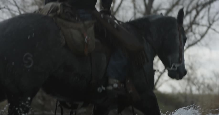 Cowboy riding a horse down a shallow stream on a cloudy winter day