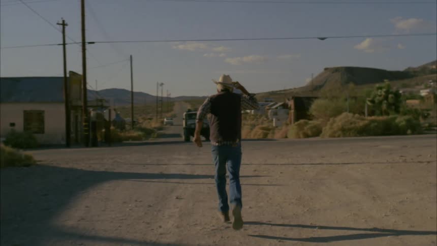 An elderly man with a cowboy hat flags down the attention of a moving vehicle