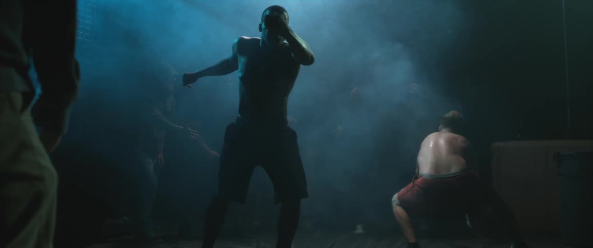 Men fighting in a dark area while others watch