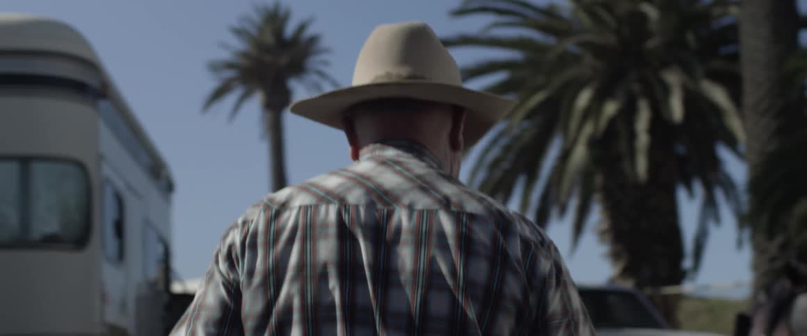 Man wearing cowboy hat walking outside toward horses