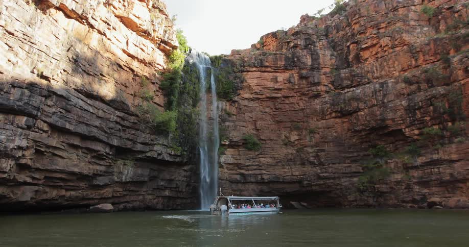 A tour boat travels next to a waterfall
