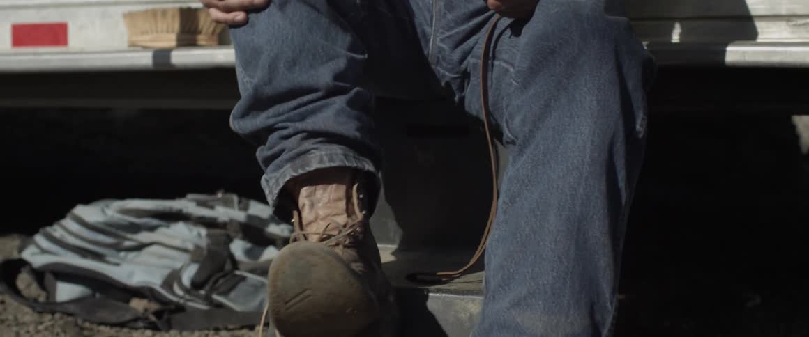 A man sitting on a step stool outside takes off his work boot