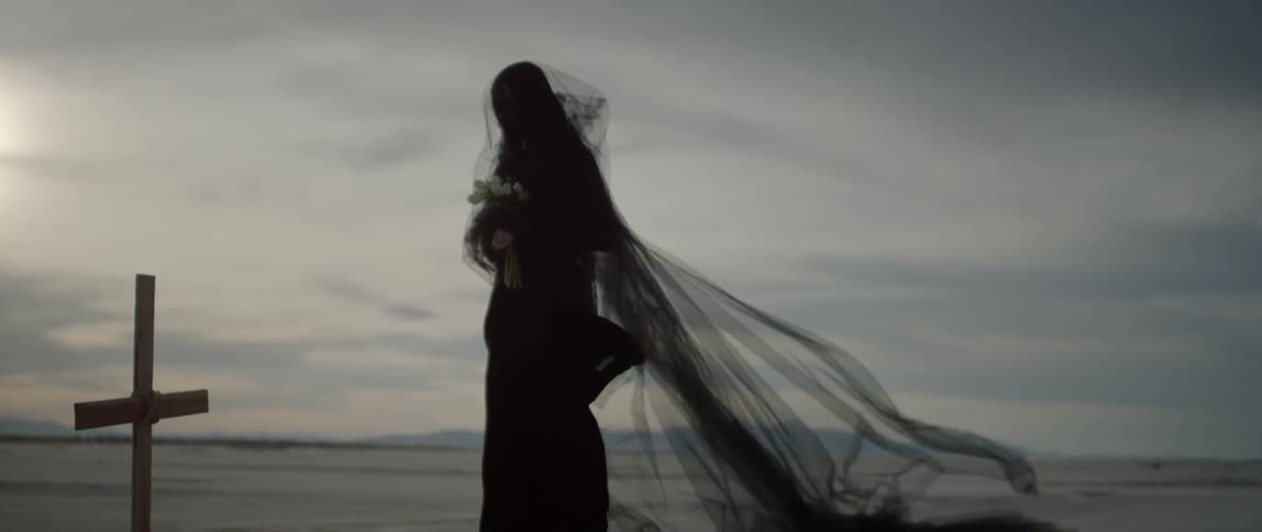 A woman grieves at a cross wearing black lace