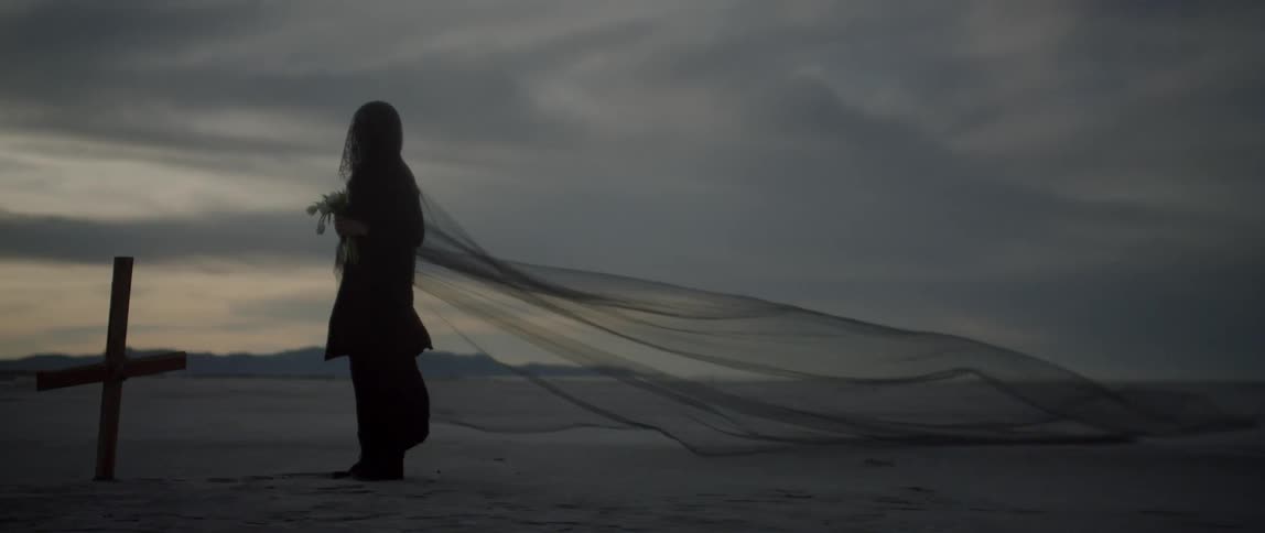 A woman wearing a lace dress grieves as the wind blows