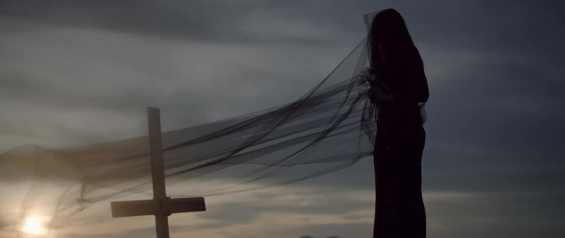 Woman wearing a long black veil stands next to a grave