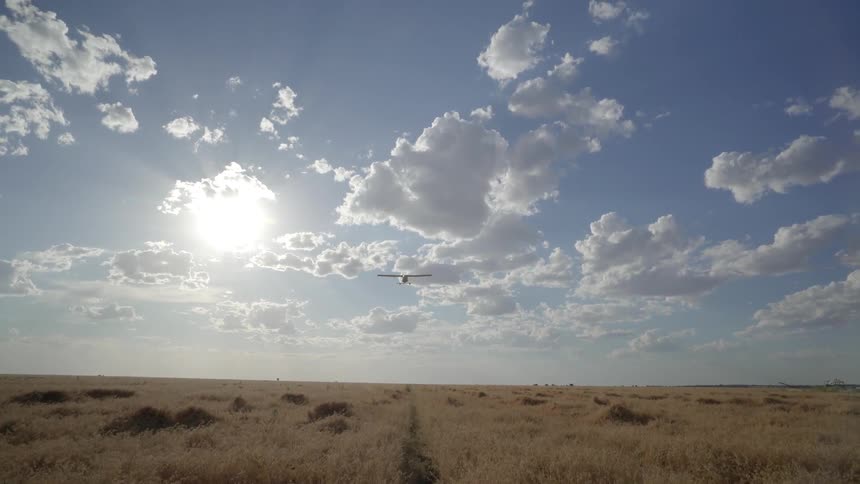 Airplane flies over plains on a sunny day