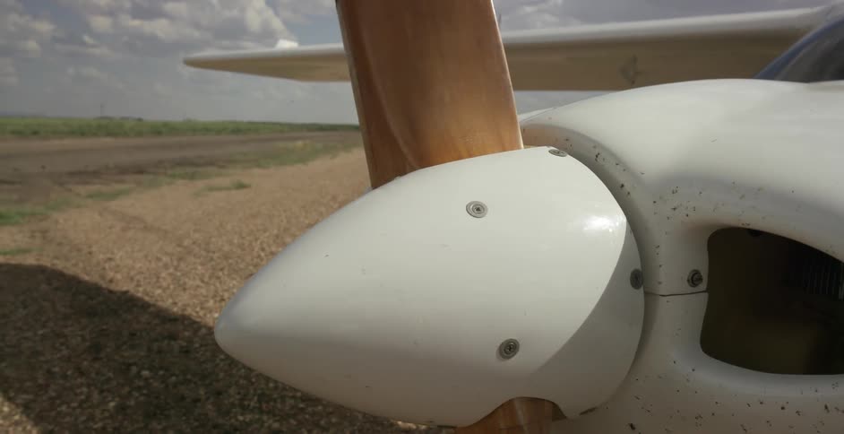 A man is turning the prop on a single engine plane as it sits on the ground