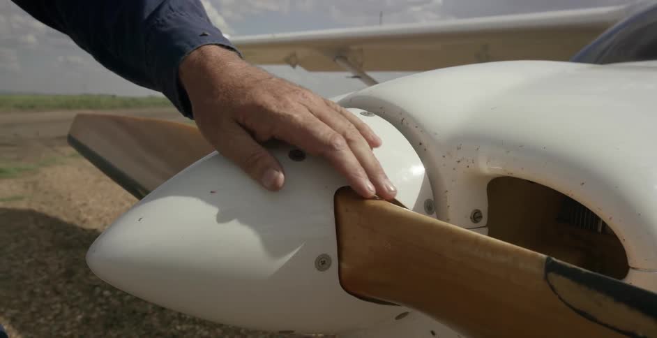 A person runs their hand along the propeller of a small airplane
