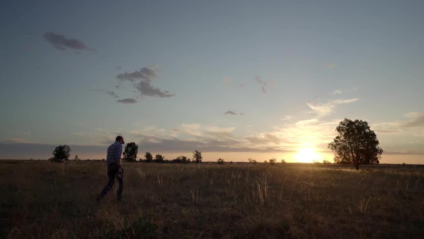 A man carrying a camera walks through a field at sunset
