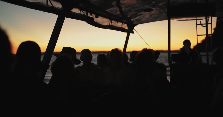 Many people sit on a boat at sunset