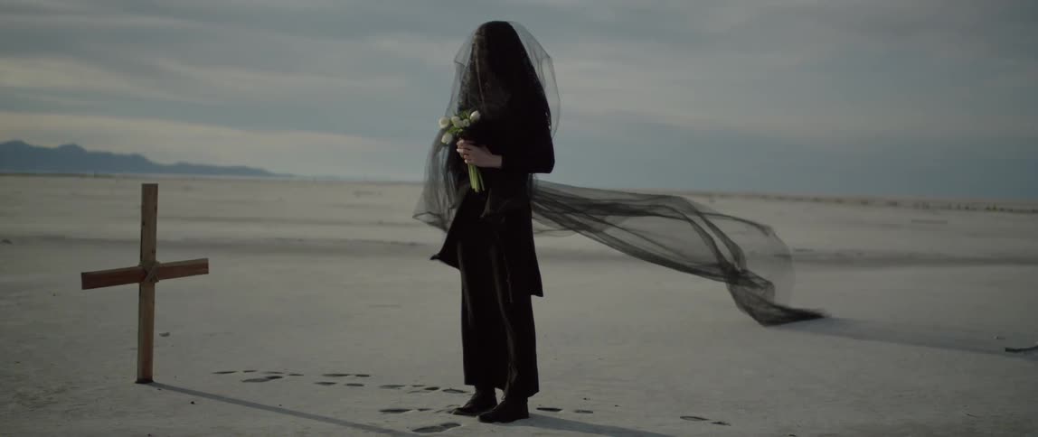 A woman grieves at a cross wearing black lace