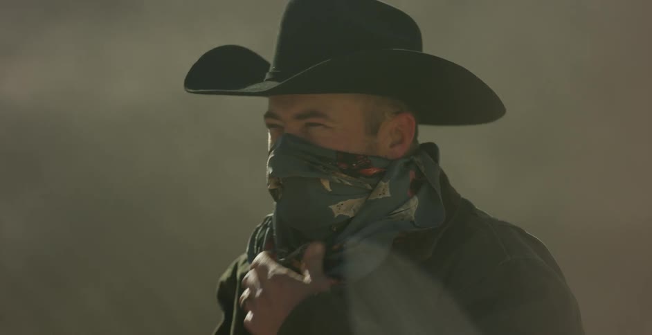 A cowboy covers his mouth and nose with a bandana