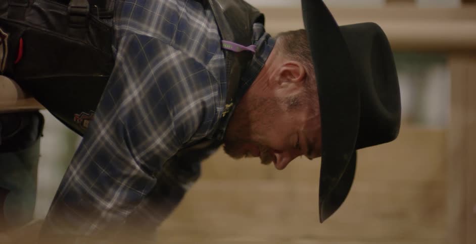 A cowboy leans down towards something